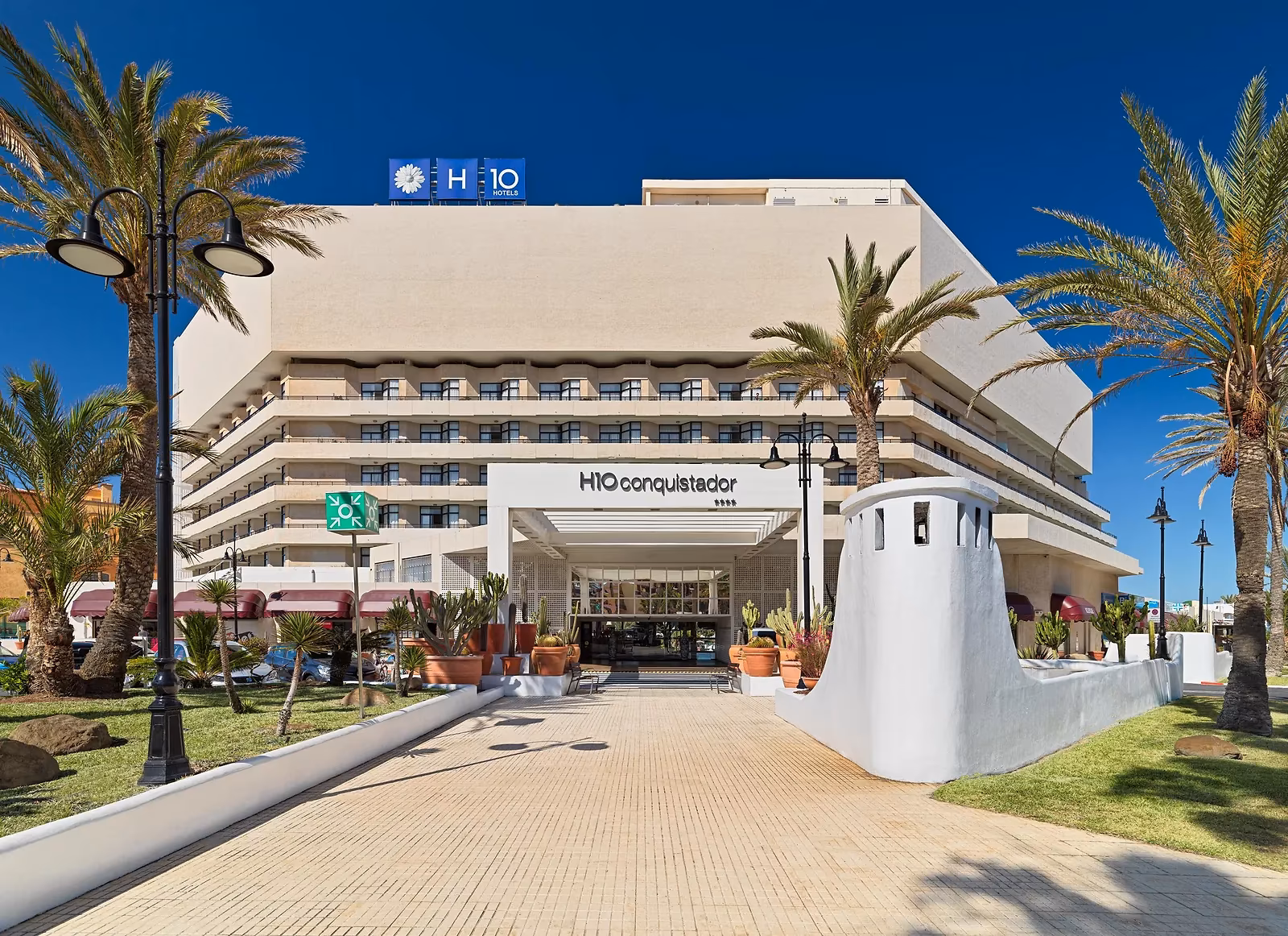 Hoofdingang met het H10-bord, een tegelpad en palmen bij H10 Conquistador in Playa de las Américas