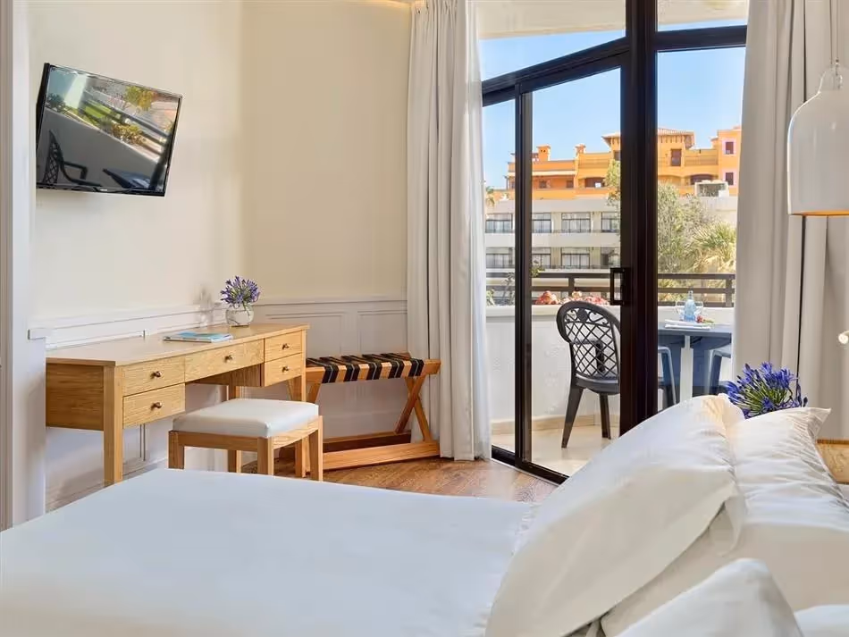 Kamer met een bed, een houten bureau, balkondeuren en uitzicht op de omgeving bij H10 Conquistador in Playa de las Américas
