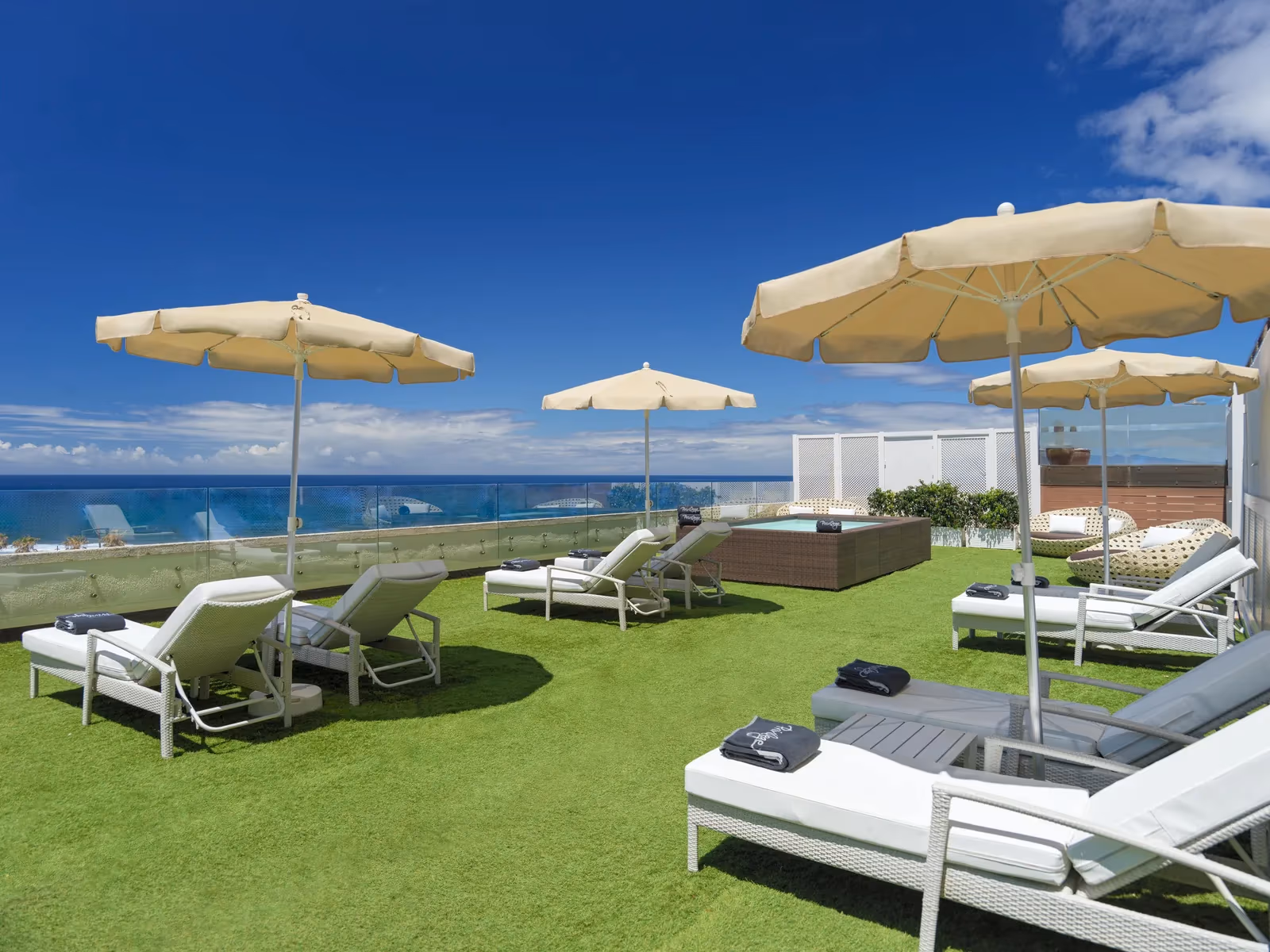 Gazonterras met witte ligbedden, parasols en een bubbelbad met uitzicht op zee bij H10 Conquistador in Playa de las Américas
