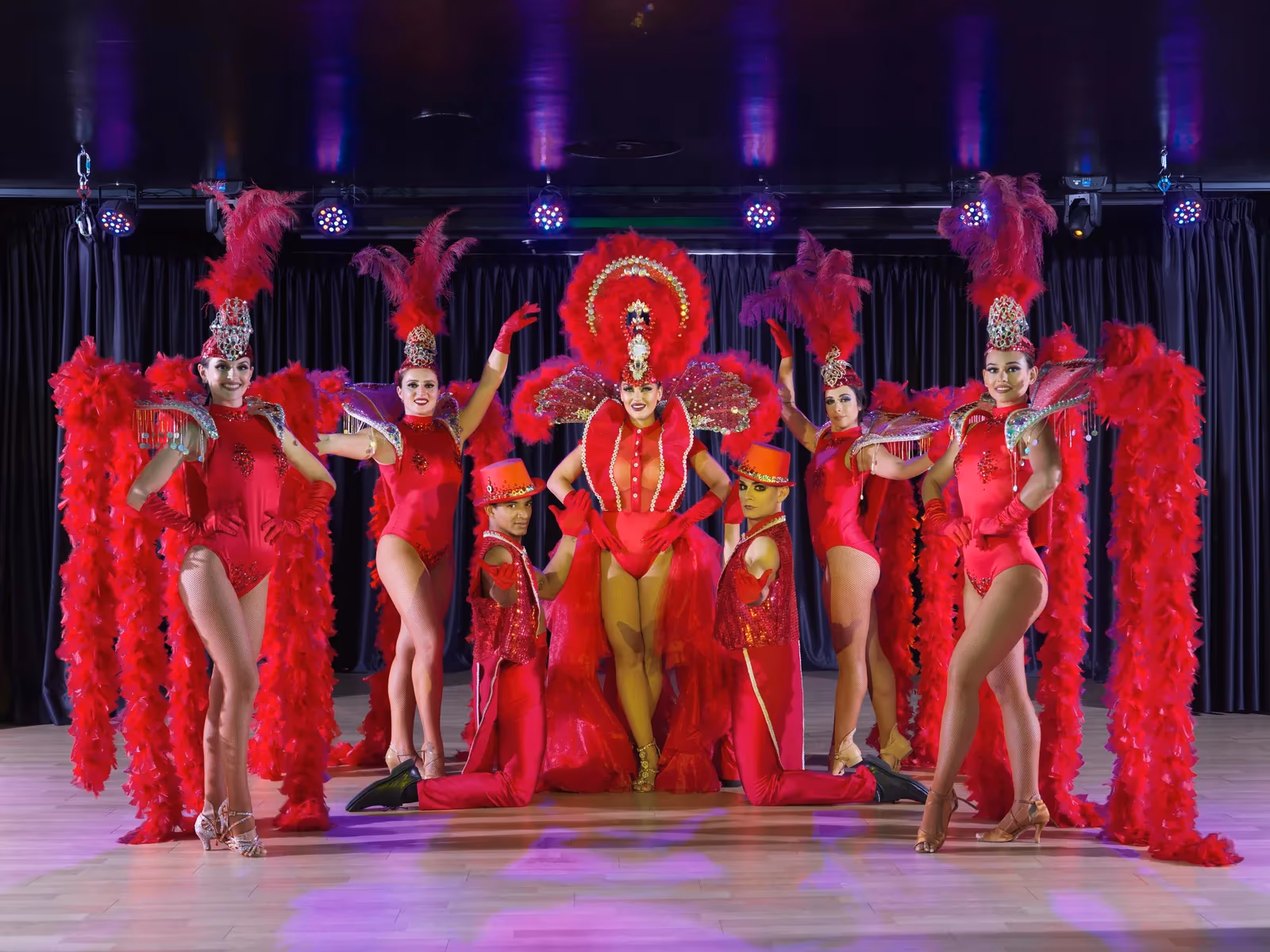 Dansers in rode kostuums met veren op een podium voor een zwart gordijn bij H10 Conquistador in Playa de las Américas