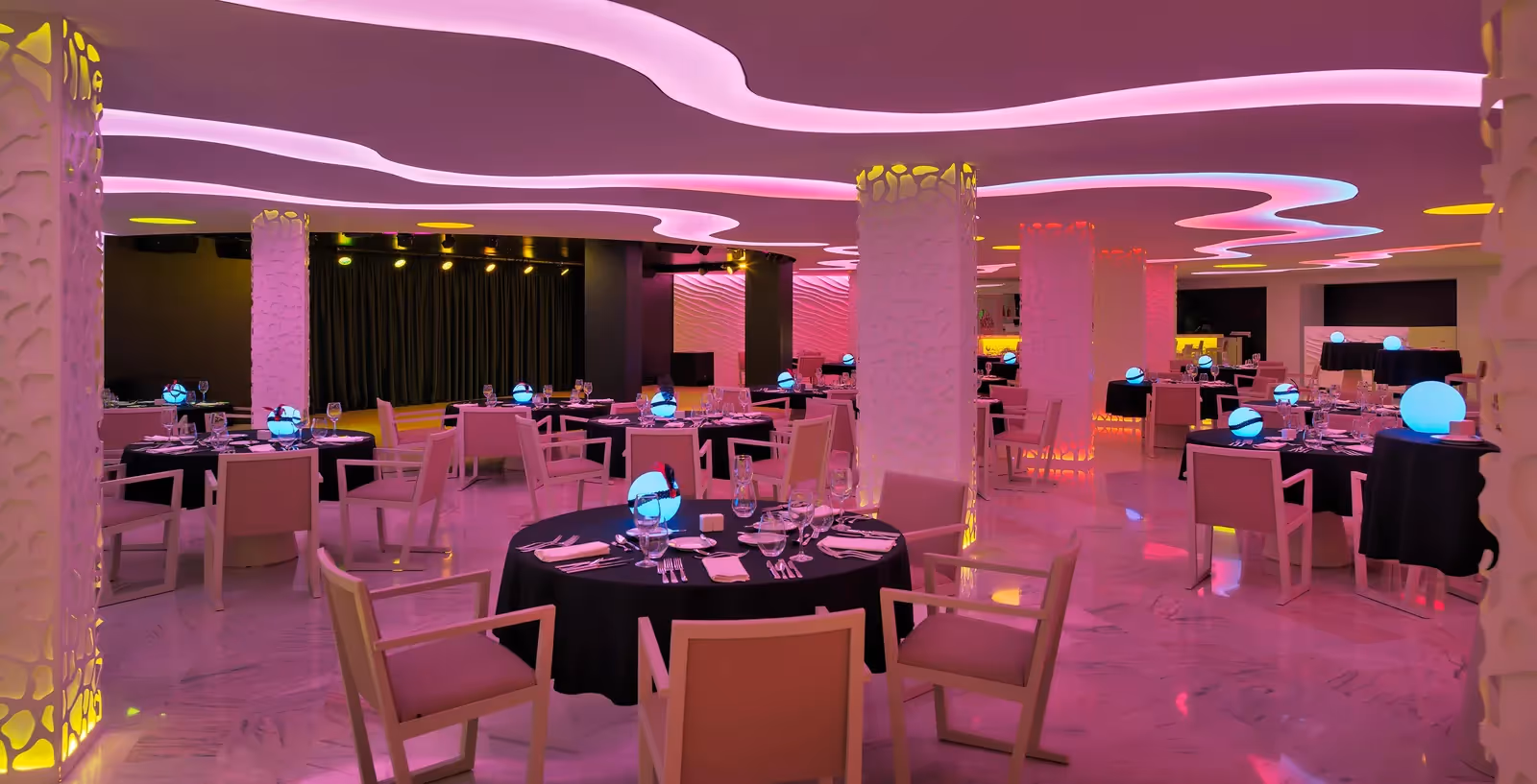 Zaal met gedekte ronde tafels met zwarte kleden en roze plafondverlichting bij H10 Conquistador in Playa de las Américas