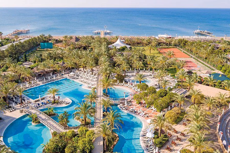 Het zwembadlandschap met palmen bij Hotel Royal Wings in Lara, met de zee op de achtergrond